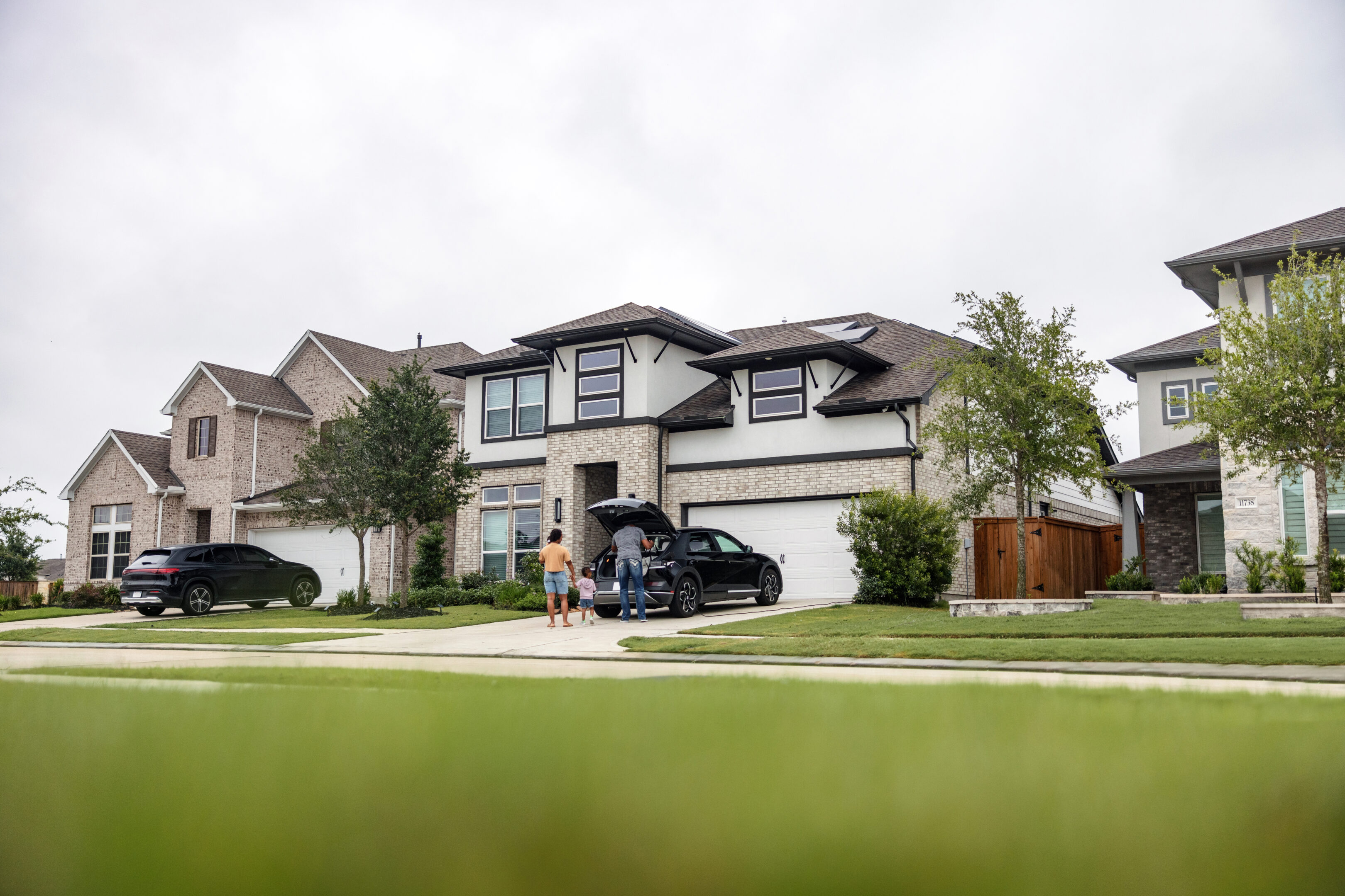 A joyful multiethnic family arrives home and charges their electric vehicle (EV) in front of their house equipped with solar panels. The scene depicts sustainable living and togetherness