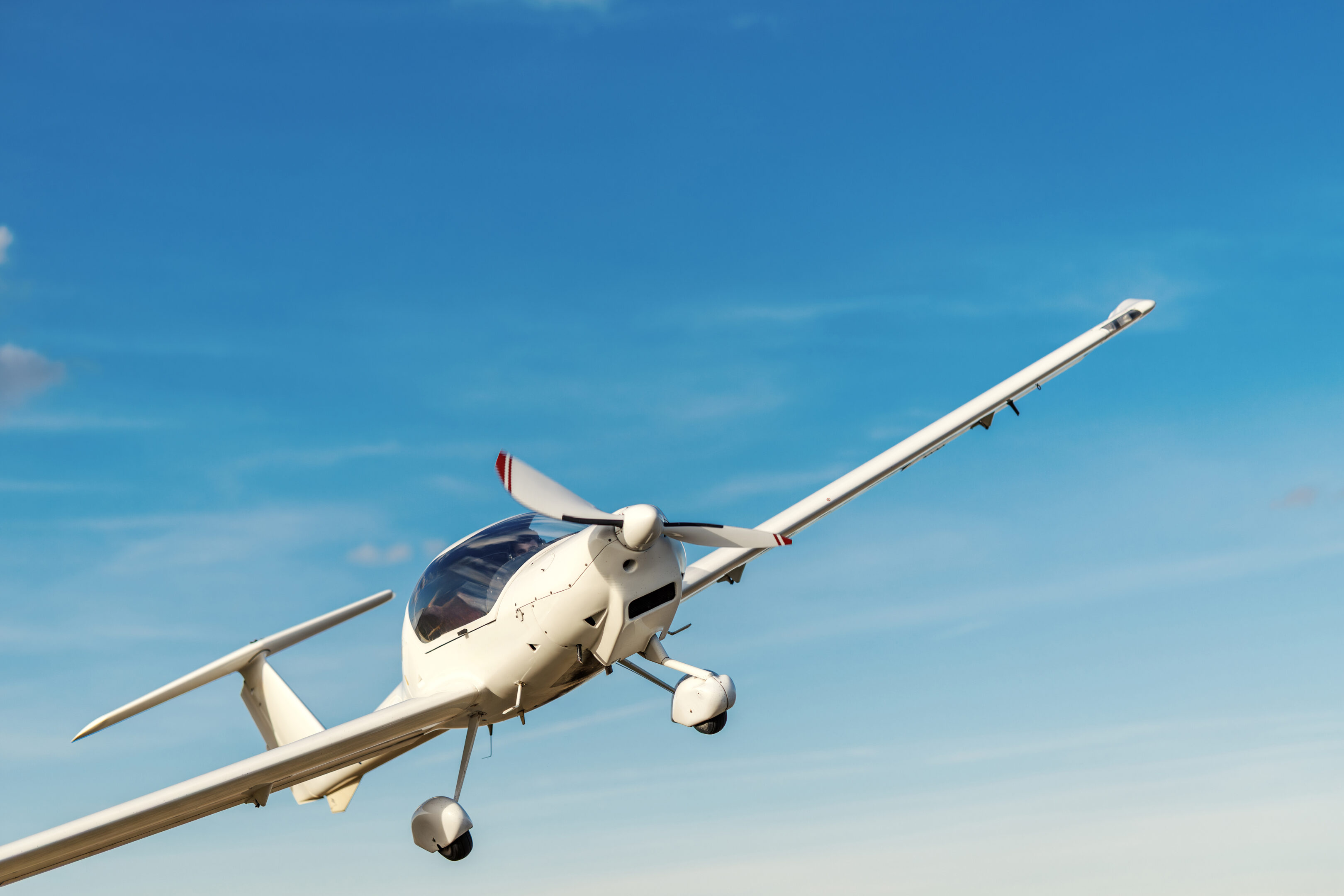 White modern propeller plane climbing into a clear blue sky, symbolizing aviation, freedom, adventure and progress while cruising above sunlit clouds on a bright day
